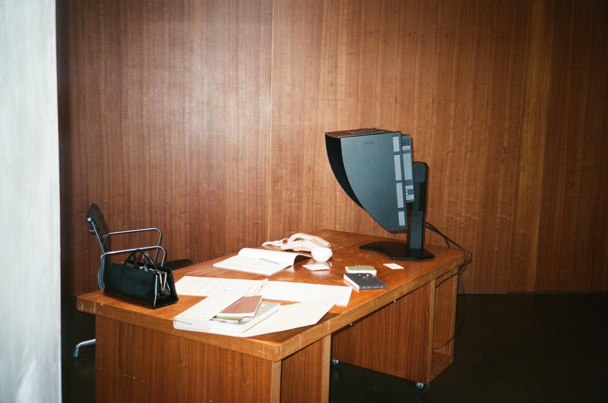 Wooden desk with computer monitor, chair, and papers against a wooden wall.