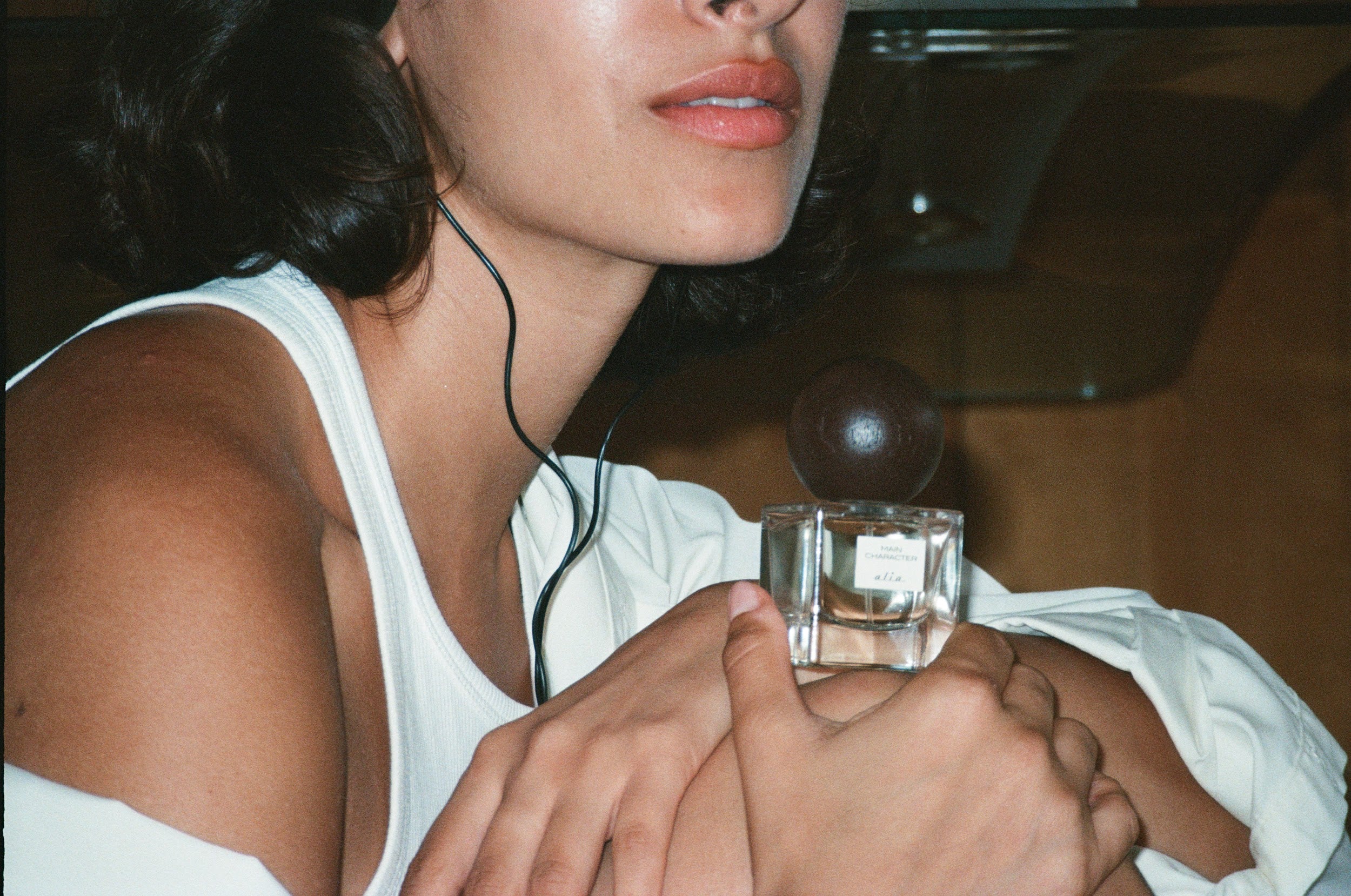Person holding a glass bottle of'Main Character' whilst wearing black headphones