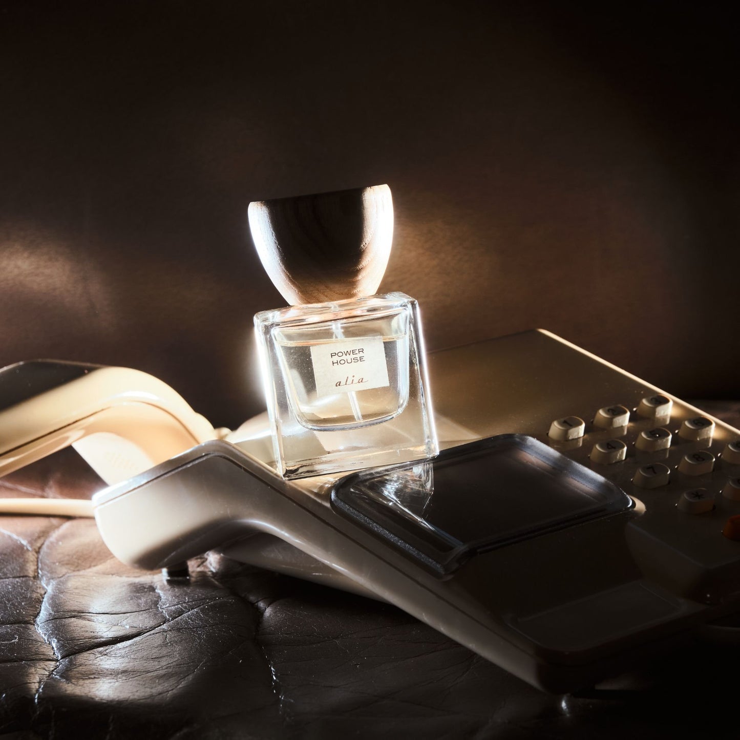 Perfume bottle balancing on a vintage telephone with a dark background