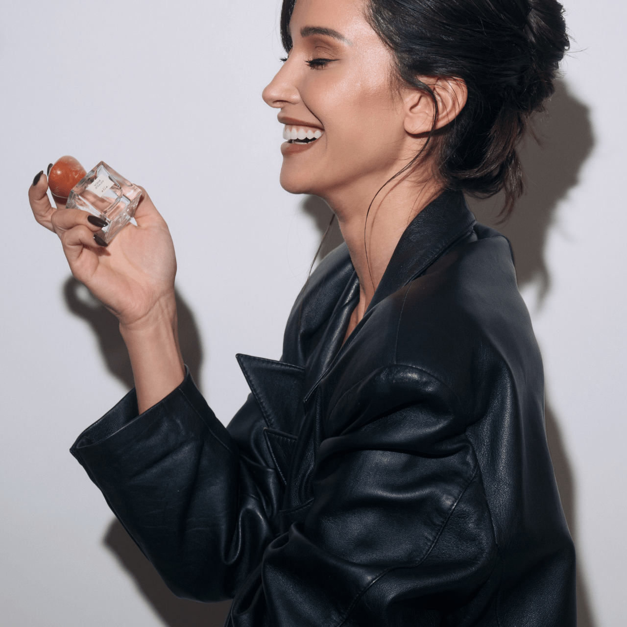 Founder of Alia, Roxie Nafousi, holding a bottle of Scene Stealer perfume and laughing